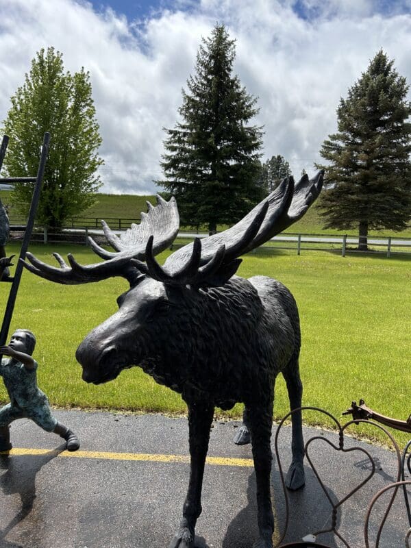 A moose statue is standing in the middle of a road.