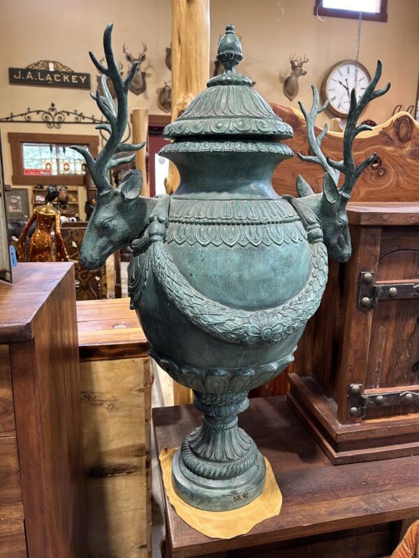 A large green urn with two deer heads on top of it.