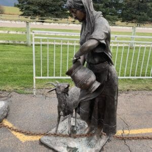 A statue of a woman and goat in the middle of a road.